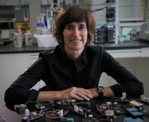 University of Utah chemical engineering associate professor Kerry Kelly. A woman with brown hair and a dark blouse who is sitting with electronic parts in front of her on a desk