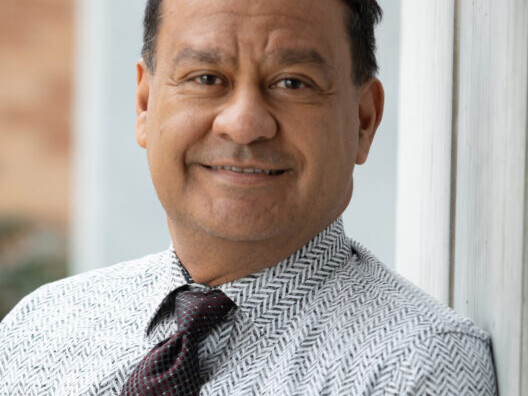Latino man with black hair wearing a white and gray chevron button-up shirt