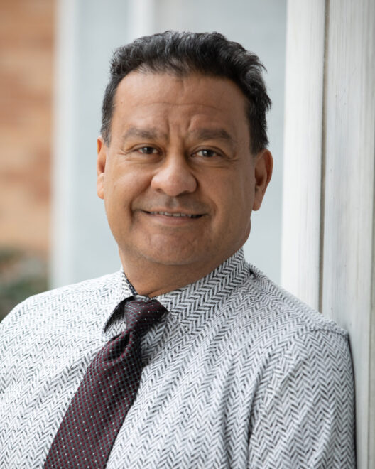 Latino man with black hair wearing a white and gray chevron button-up shirt