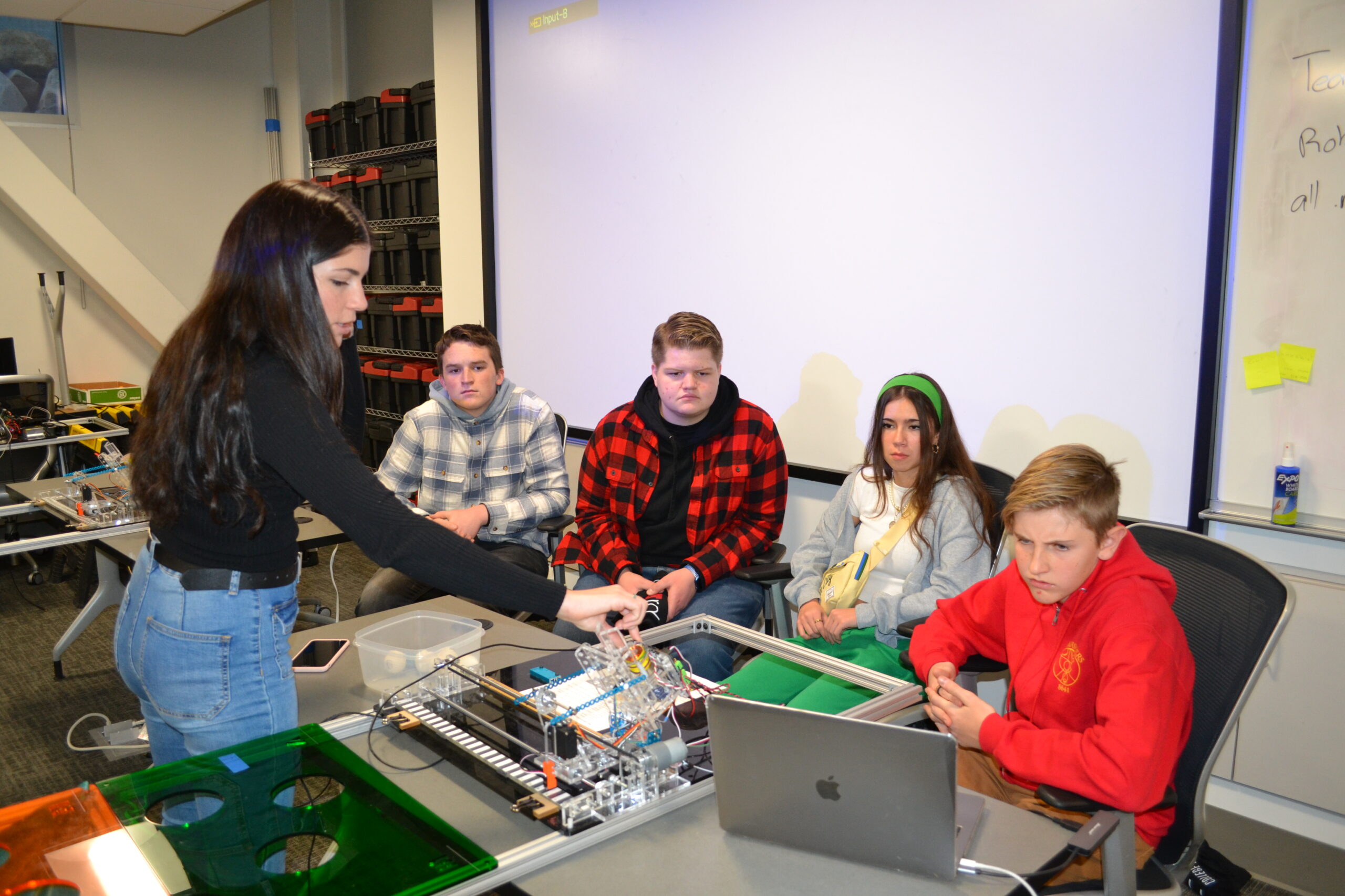 White woman with black hair shows four students electrical board