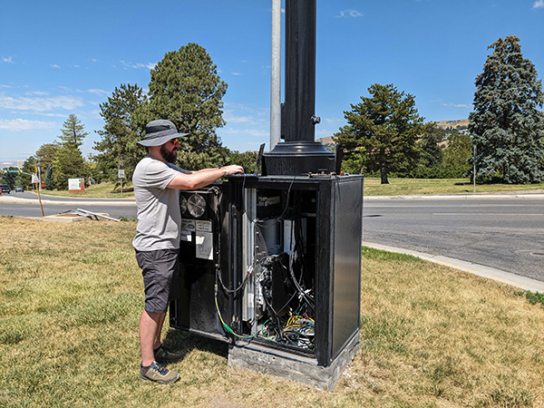 Researcher Dustin Maas types on a laptop plugged into equipment installed in the base of a streetlight. 