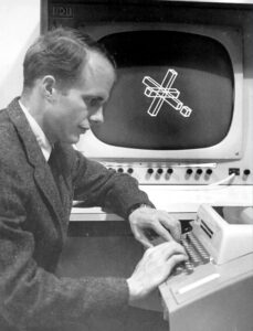 A 1968 black and white photo of John Warnock sitting at a keyboard with a simple computer display behind him. 