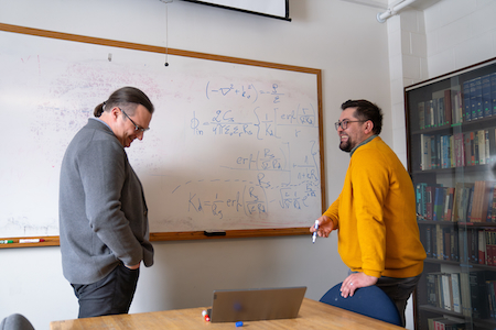 Two men share a laugh as they work together in front of a whiteboard.