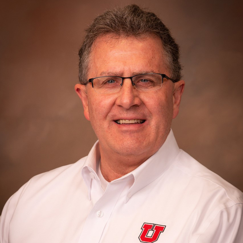 Headshot of Larry Milner. He is posed against a neutral background is a white Utah branded polo shirt