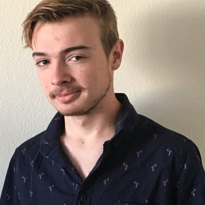 Headshot Sam Makin, outstanding Undergraduate research 2025 recipient. He is in a dark blue chirt against a white background wall
