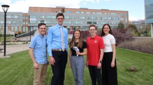 A team of five students poses outside with their handheld device