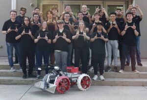 Utah Student Robotics pose, all making the U sign, while standing behind their robot.